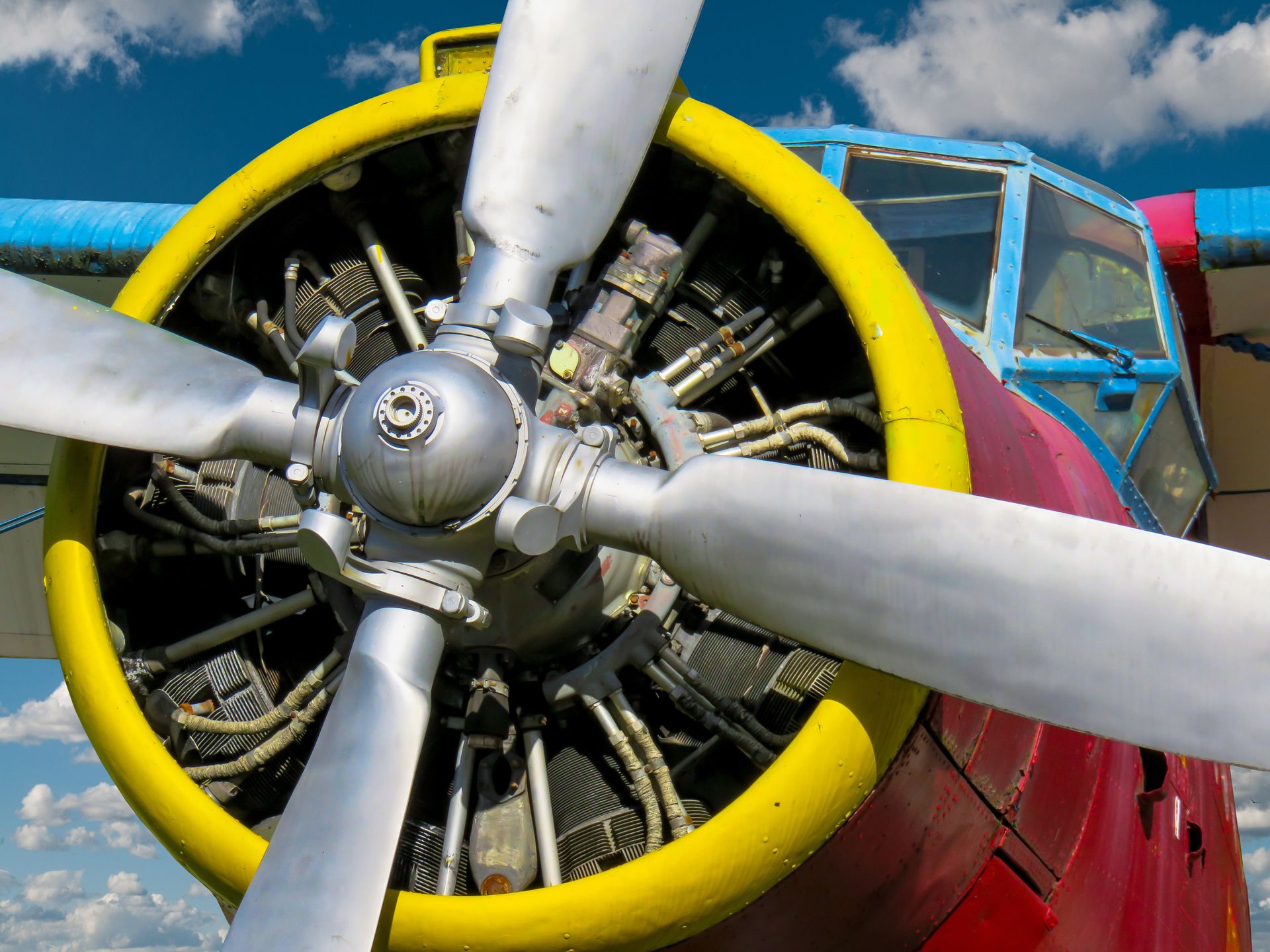 Detailed view of a colorful vintage propeller airplane with a focus on the engine and propellers, set against a blue sky.