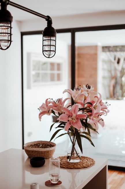 A beautiful vase of pink lilies on a modern kitchen table near a window.