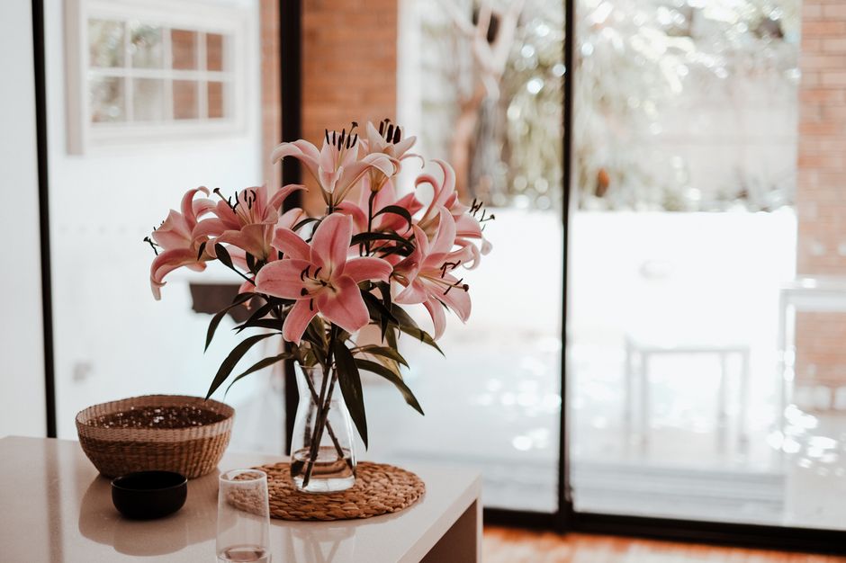 A beautiful pink lily bouquet in a vase on a table in a bright, modern room with large windows.