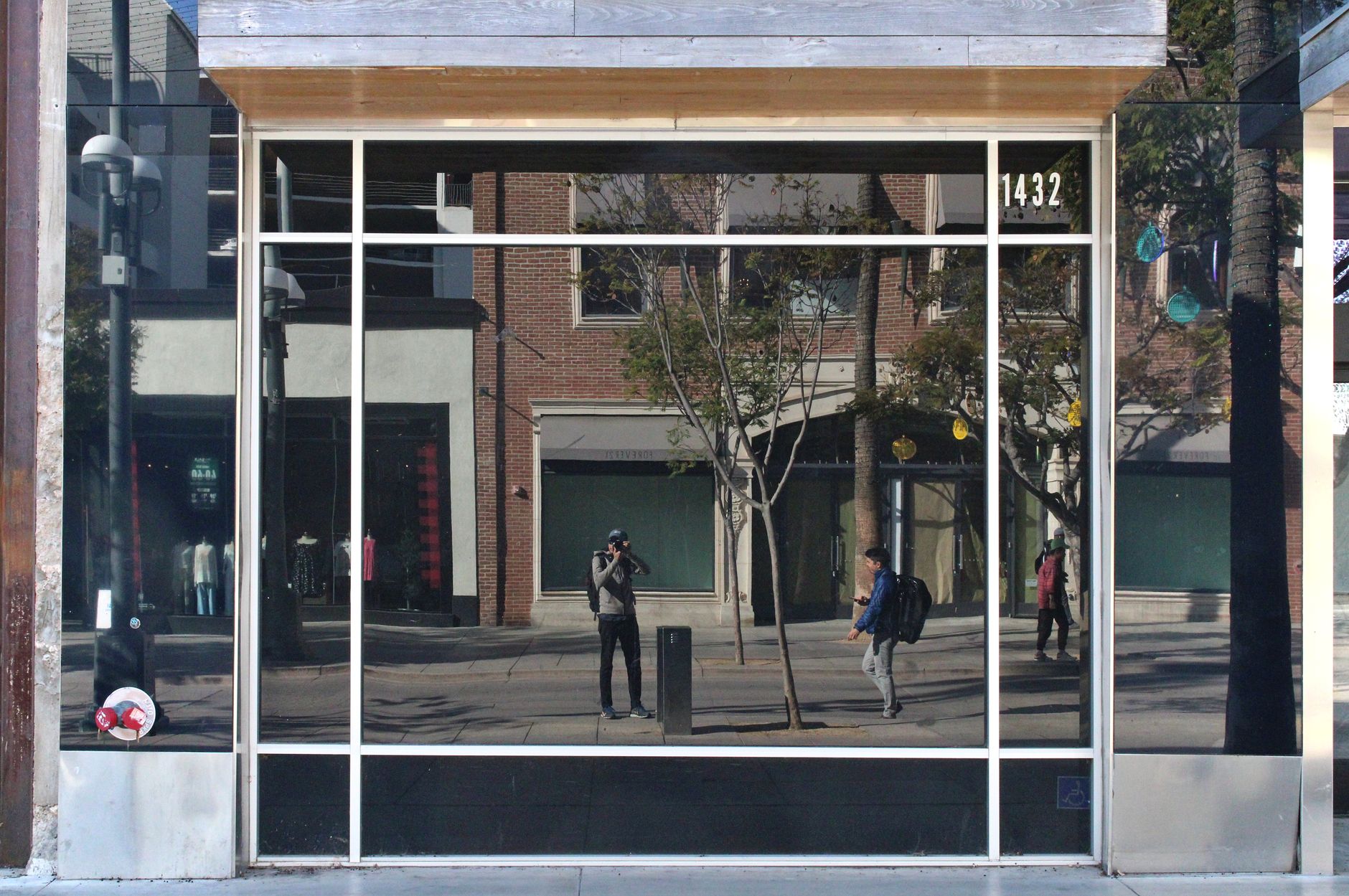 A city street reflected in a glass storefront facade, capturing pedestrians and urban architecture.