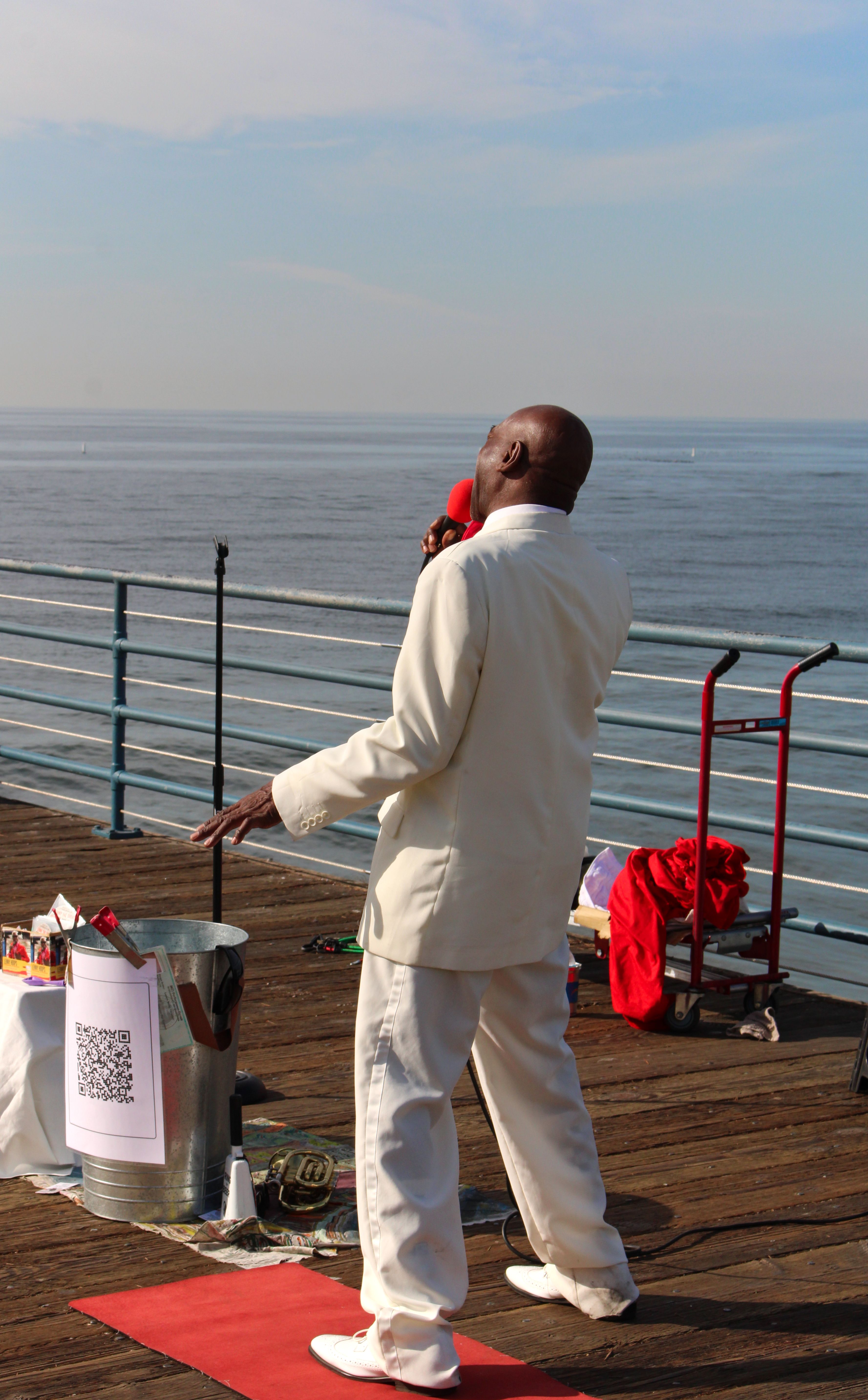 Solo street performer in white outfit sings passionately on a scenic seaside pier.