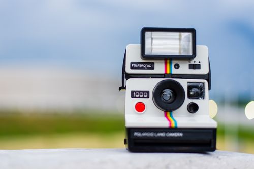 Free Vintage instant camera with rainbow stripe detail on a blurred outdoor background. Stock Photo