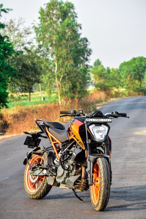 Free Orange motorcycle parked on a rural road in Nandurbar, India surrounded by lush greenery. Stock Photo
