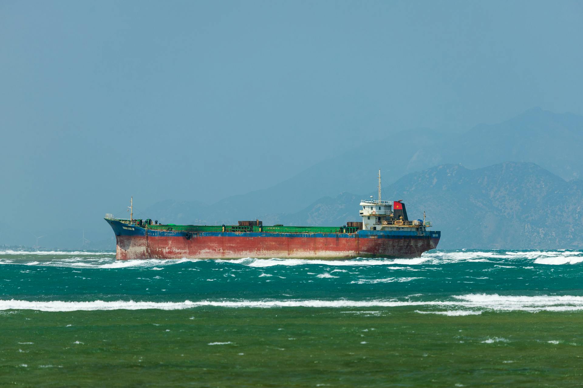 A large cargo ship sails on a choppy sea with mountains in the background, showcasing transportation at sea.