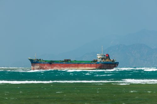 Free A large cargo ship sails on a choppy sea with mountains in the background, showcasing transportation at sea. Stock Photo