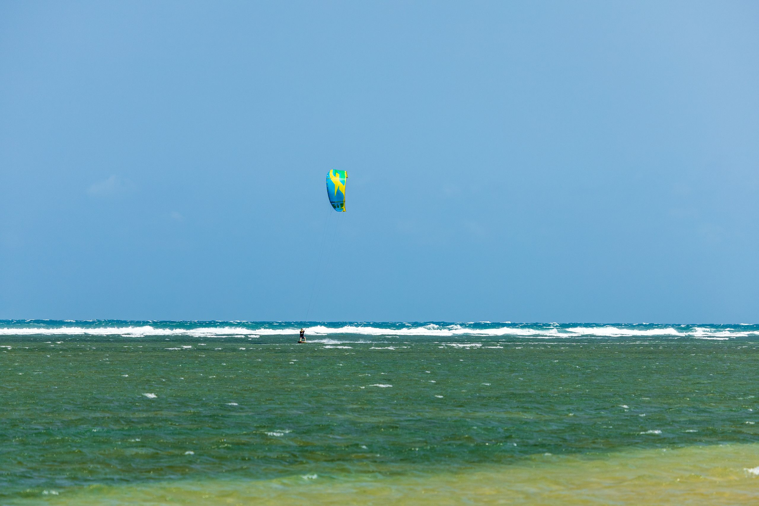 Pessoa praticando kite surf na praia, simbolizando liberdade, aventura e esportes aquáticos ao ar livre.