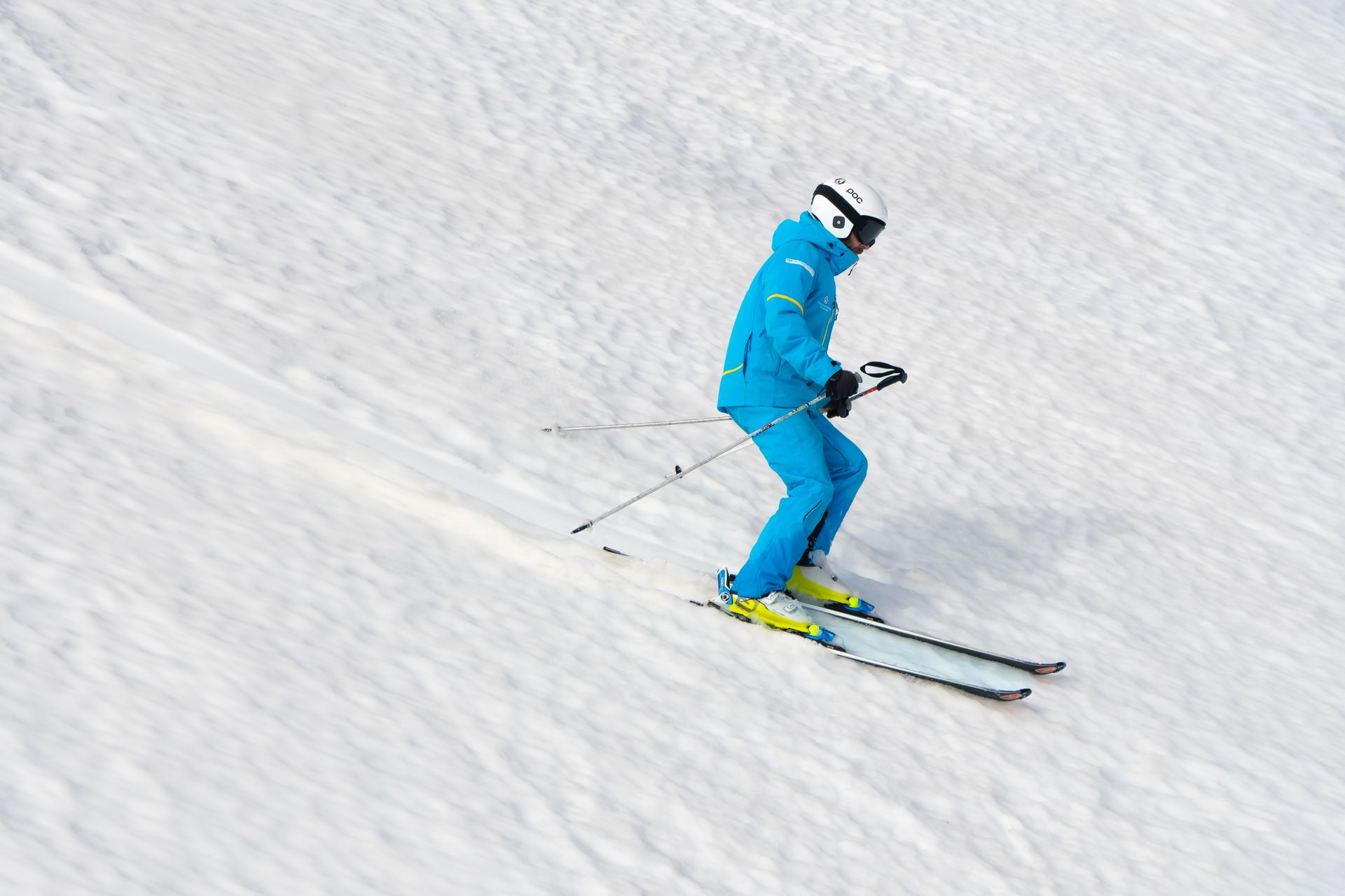 A skier in blue gear skiing downhill on a snowy slope during winter, showcasing dynamic motion.