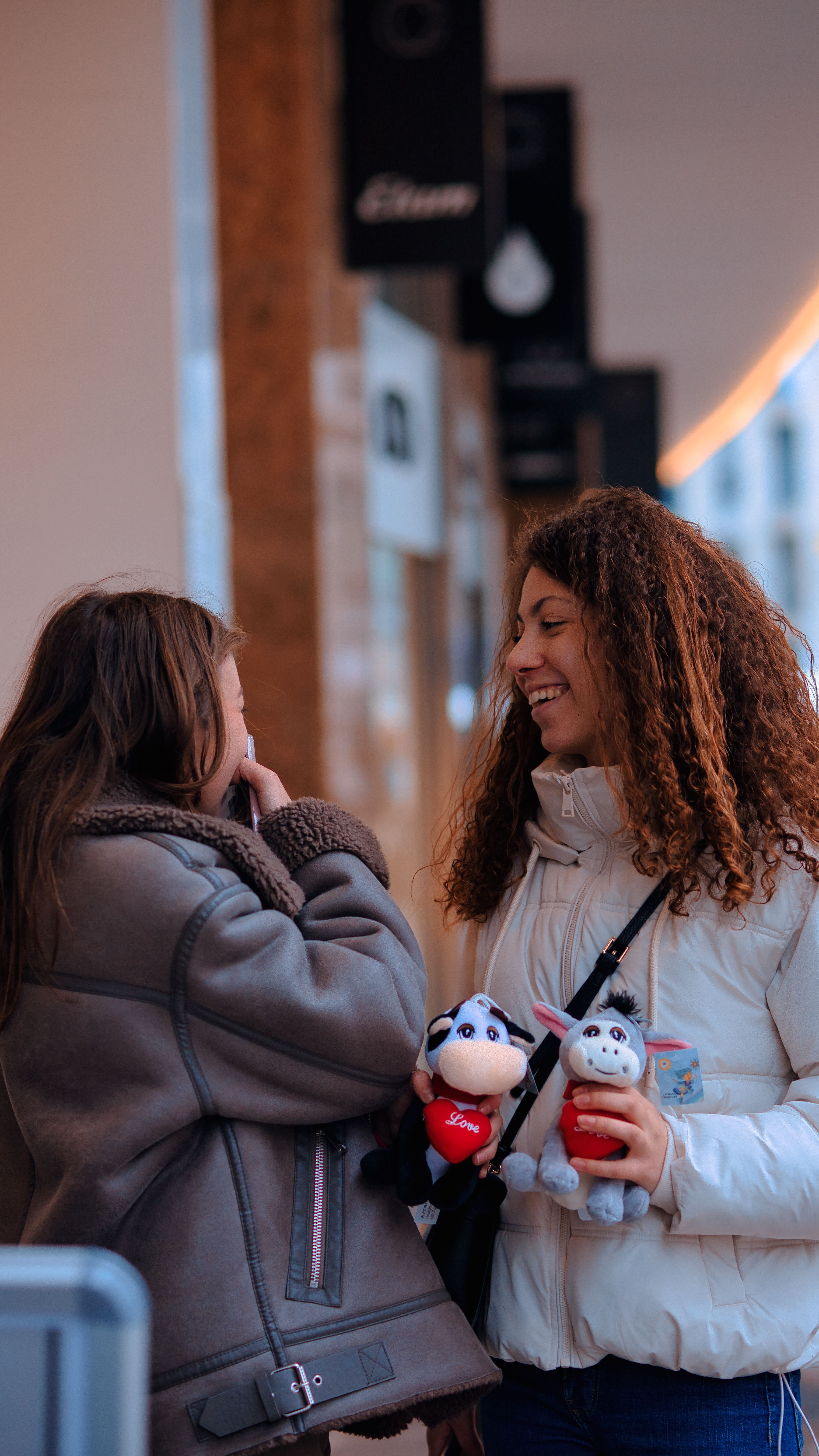 Two women enjoying a candid moment in the city, holding plush toys and laughing together.