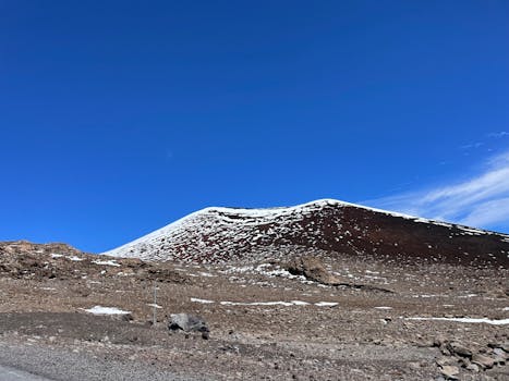 Breathtaking view of a snow-covered volcanic hill against a bright blue sky, showcasing nature's contrast.