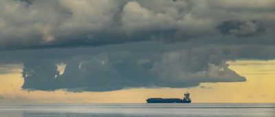 A solitary oil tanker sails across the water beneath a heavy, dramatic cloud formation.