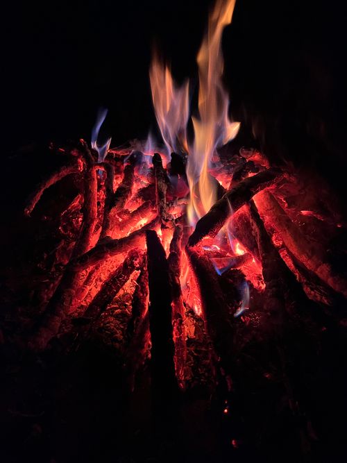 Free A close-up view of a vibrant campfire with bright orange and blue flames illuminating charred wood against a dark backdrop. Stock Photo