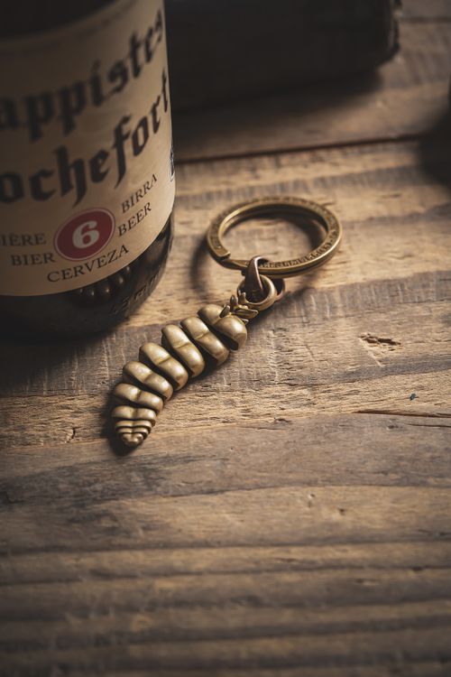 Free A vintage brass keychain in the shape of a dragon tail beside a beer bottle on a rustic wooden surface. Stock Photo