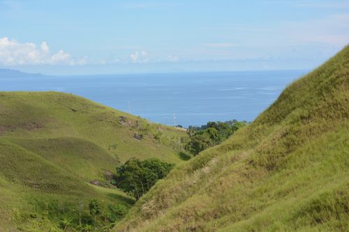 Free A serene view of green hills with the sea in the background under a clear blue sky. Stock Photo