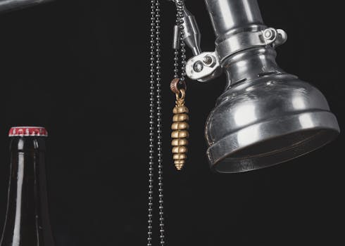Close-up of an industrial-style lamp with a golden pendant and a bottle against a black background.