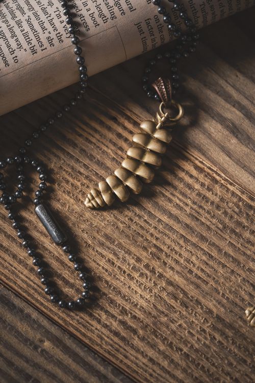 Free A detailed, artistic shot of a golden dragon tail necklace on a rustic wooden surface with a rolled newspaper. Stock Photo