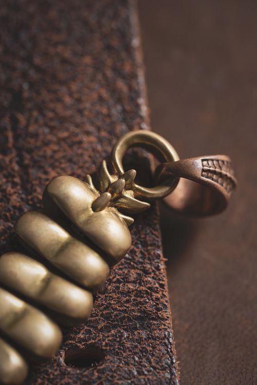 Free Intricate golden bronze handmade pendant with rich brown background, highlighted in detail. Stock Photo