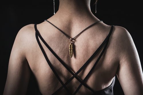 Free An artistic back view of a woman wearing a golden necklace with a stylish black strap dress. Stock Photo