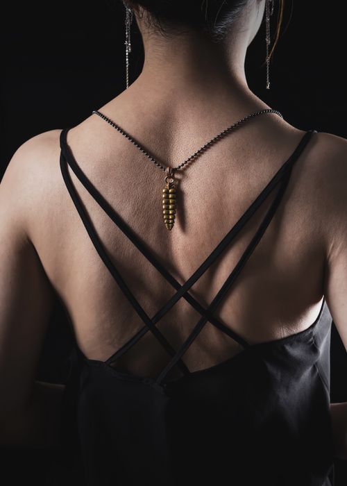 Free Back view of a woman wearing a golden necklace and chic dress in a dark setting. Stock Photo