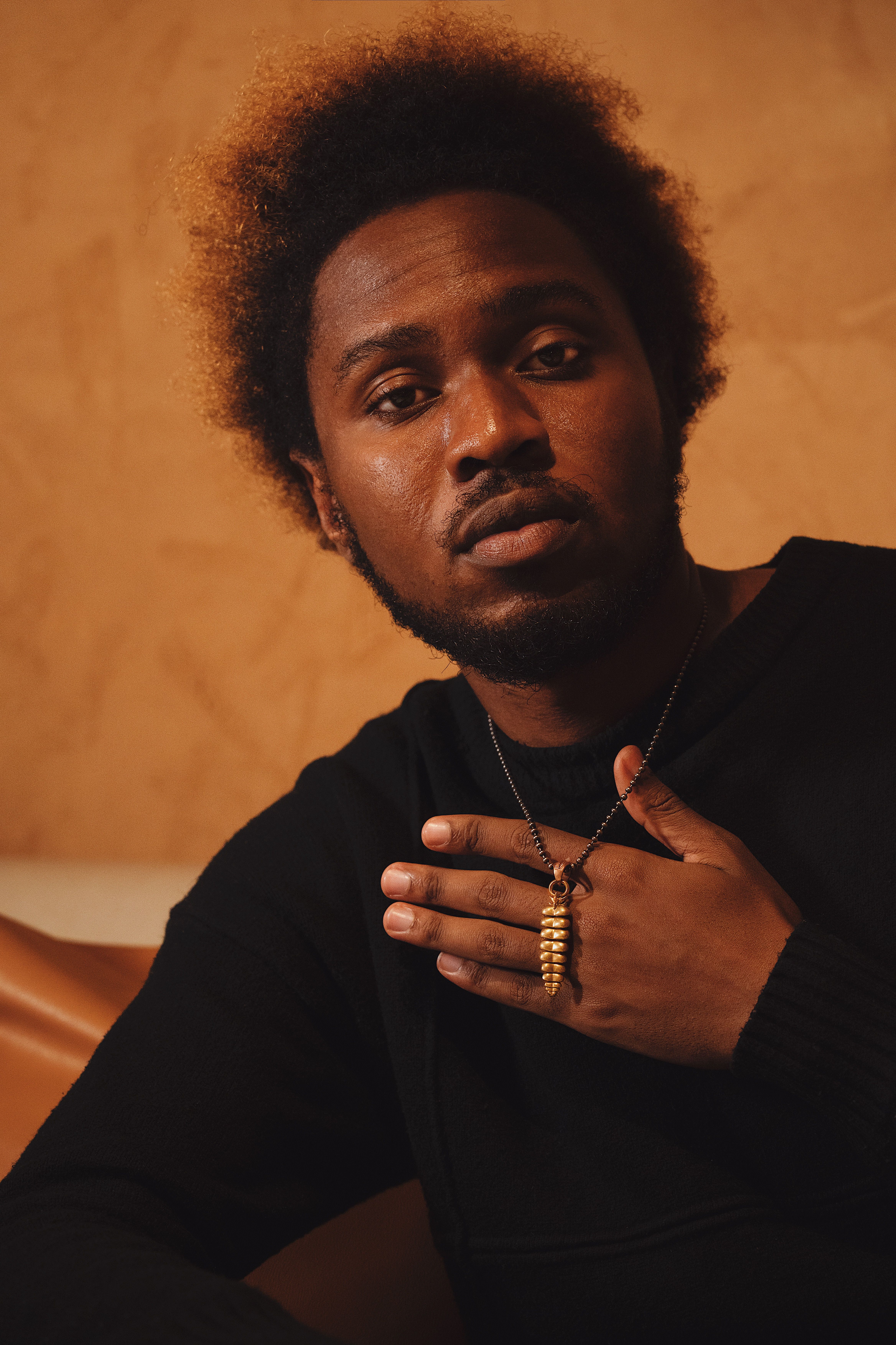 Fashion portrait of a man with a necklace against a warm background.