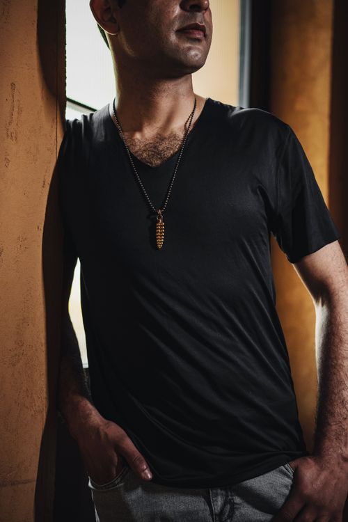 Free Portrait of a man in a black t-shirt with a dragon necklace, standing indoors. Stock Photo