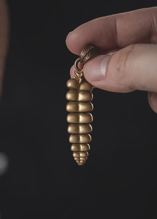 Free Intriguing golden spiral pendant held by a hand against a dark background. Stock Photo