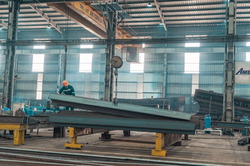 Worker guiding a steel beam inside a fabrication plant