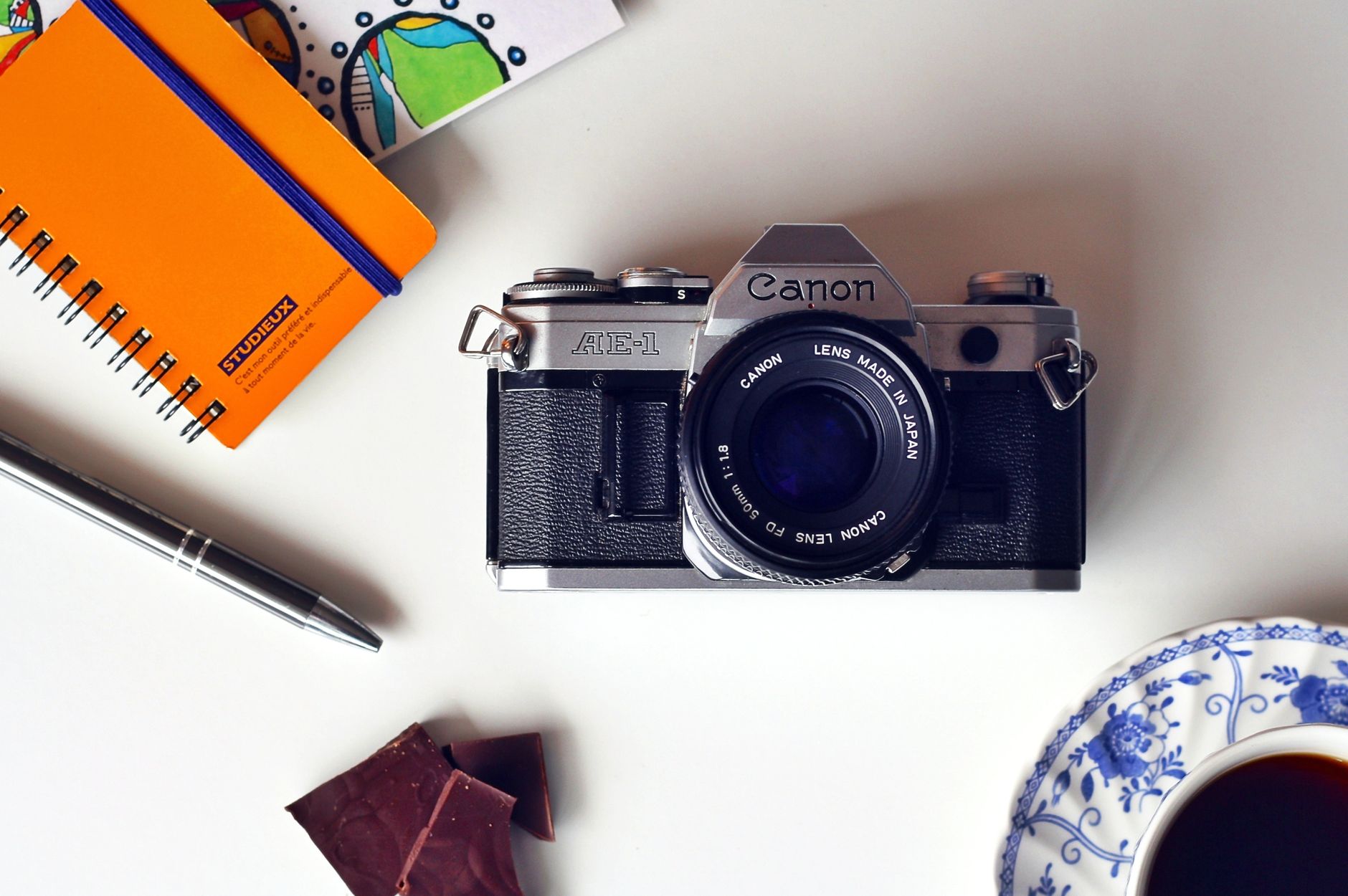 Vintage Canon camera with notepad, pen, and coffee on a desk for a creative workspace vibe.