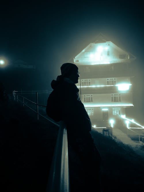 Silhouette of a Man Against an Illuminated House at Night