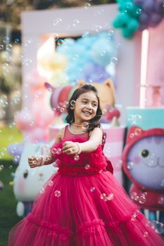 A smiling girl in a pink dress enjoys bubbles outdoors, capturing a moment of joy and playfulness.