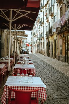 A picturesque cobblestone street in Lisbon with outdoor café tables on a spring day.