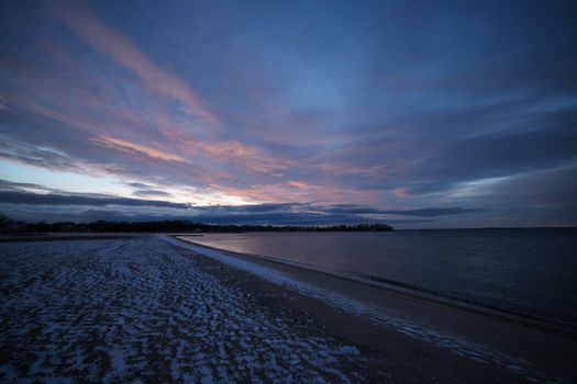 Serene winter beach scene at twilight, featuring vibrant clouds and a snow-dusted shore.