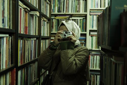Free A woman with headscarf takes a photo in a cozy bookstore filled with books. Stock Photo