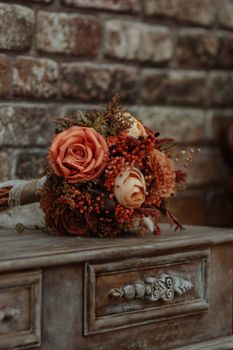 Artistic display of a vintage bouquet on a rustic dresser against a brick backdrop in warm tones.