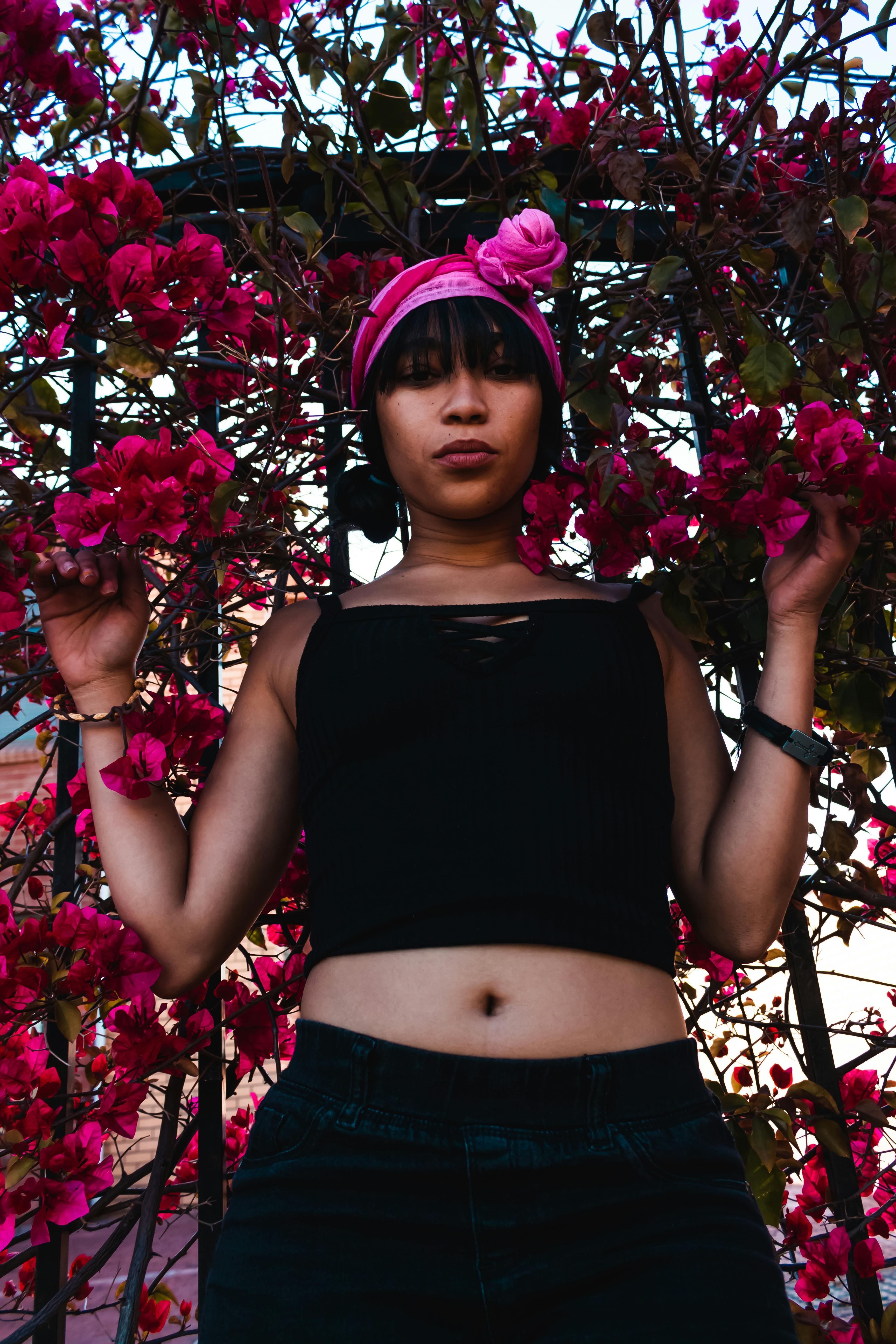 一名戴着头巾和黑色上衣的妇女，站在城市街道上，周围是充满活力的粉红色花朵