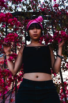 一名戴着头巾和黑色上衣的妇女，站在城市街道上，周围是充满活力的粉红色花朵