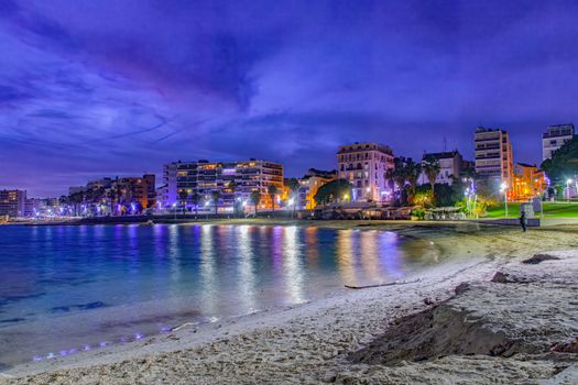 Scenic view of Toulon's beachfront at night with illuminated buildings reflecting on the sea.