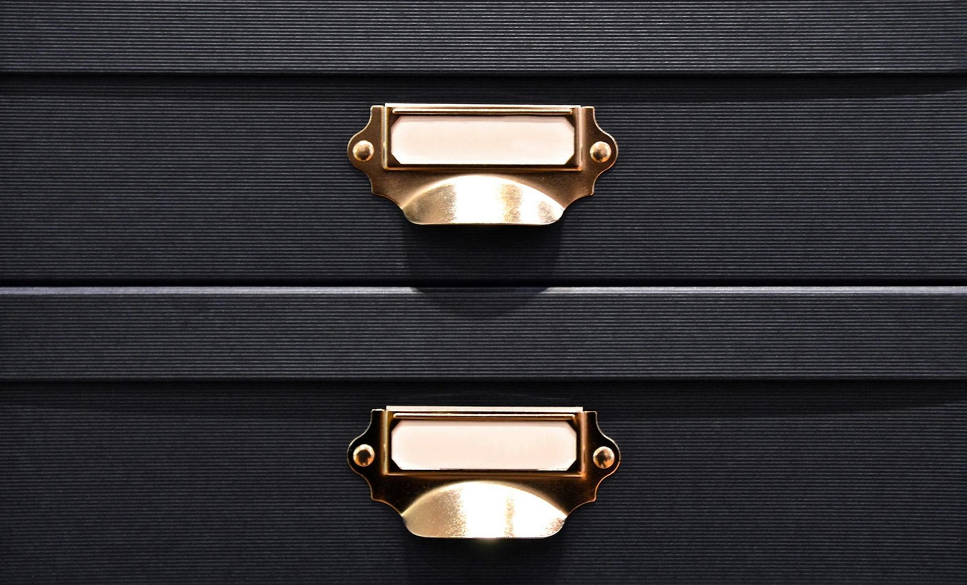 Close-up of black storage boxes featuring elegant brass handles and label holders.