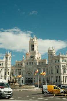 A stunning view of Palacio de Cibeles in Madrid with vibrant flags and clear blue skies.