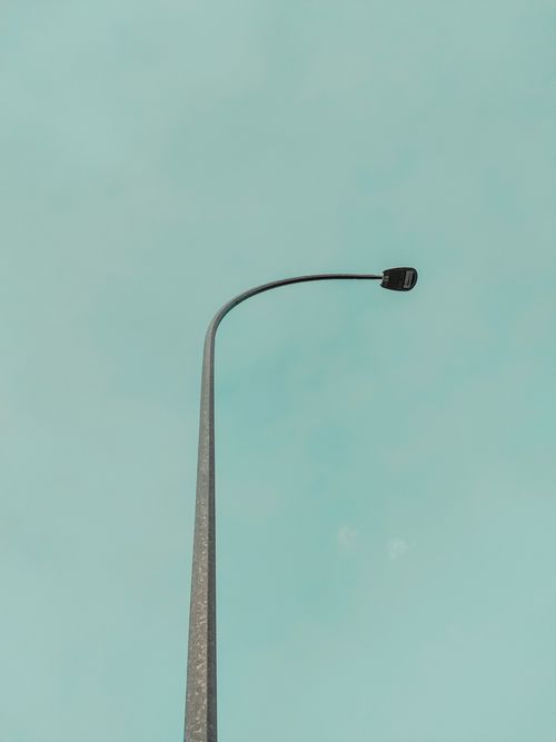 Free A bent street lamp set against a pastel blue sky, capturing urban minimalism. Stock Photo