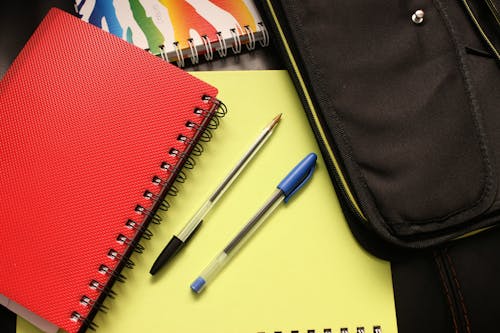 Pulpen Hitam Dan Biru Di Samping Notebook Bercakup Merah