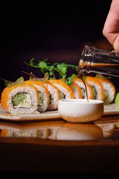 Close-up shot of delicious sushi rolls with soy sauce pouring into a dish, featuring vibrant colors.