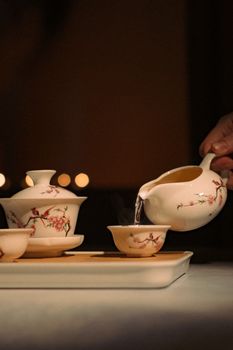 Close-up of a hand pouring tea into a delicate floral teacup in a serene setting.