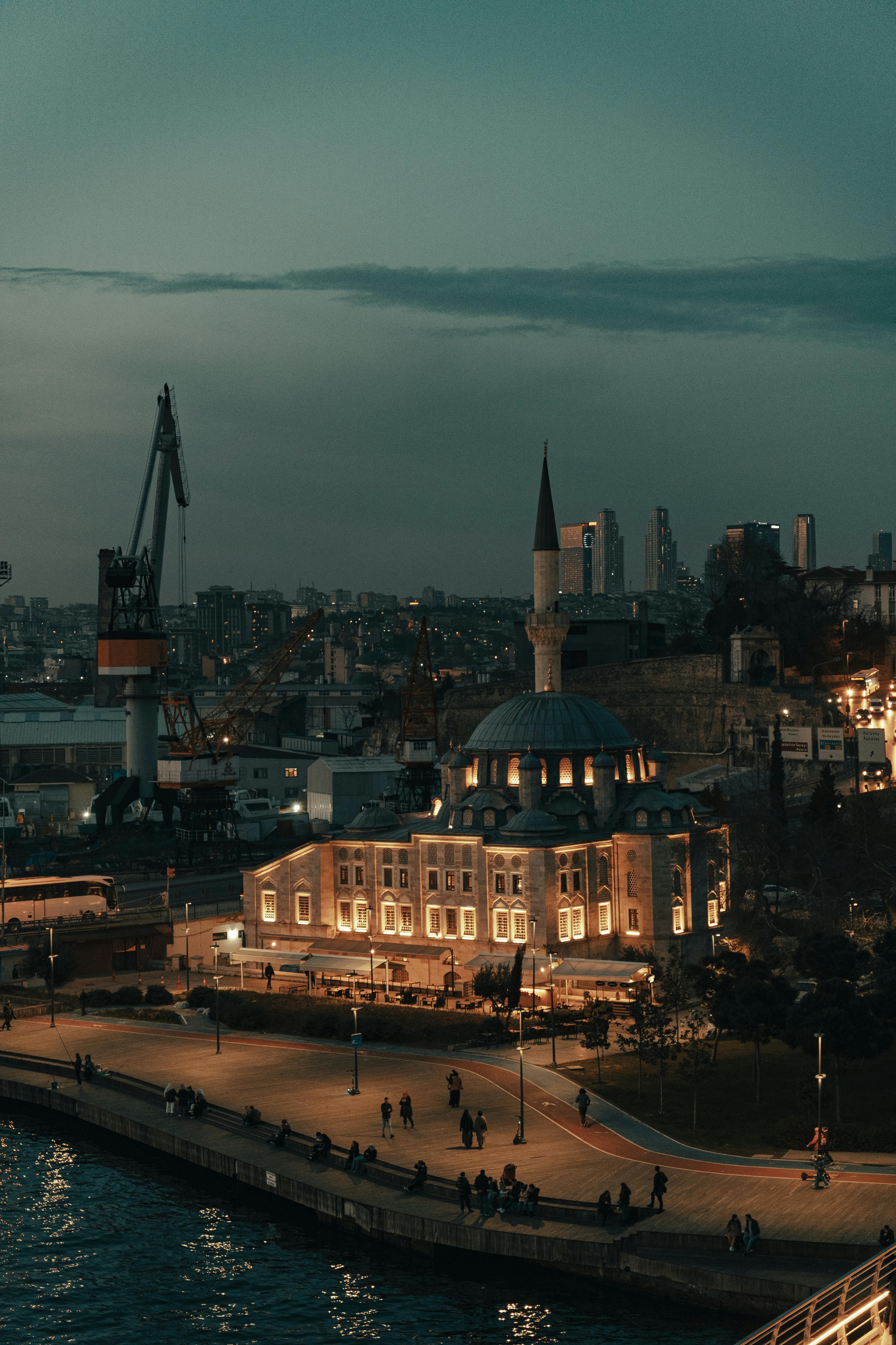 Dramatic twilight view of an illuminated mosque by the waterfront in Istanbul cityscape.