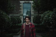 一个穿着红色格子衬衫的年轻人，带着顽皮的表情站在花园里