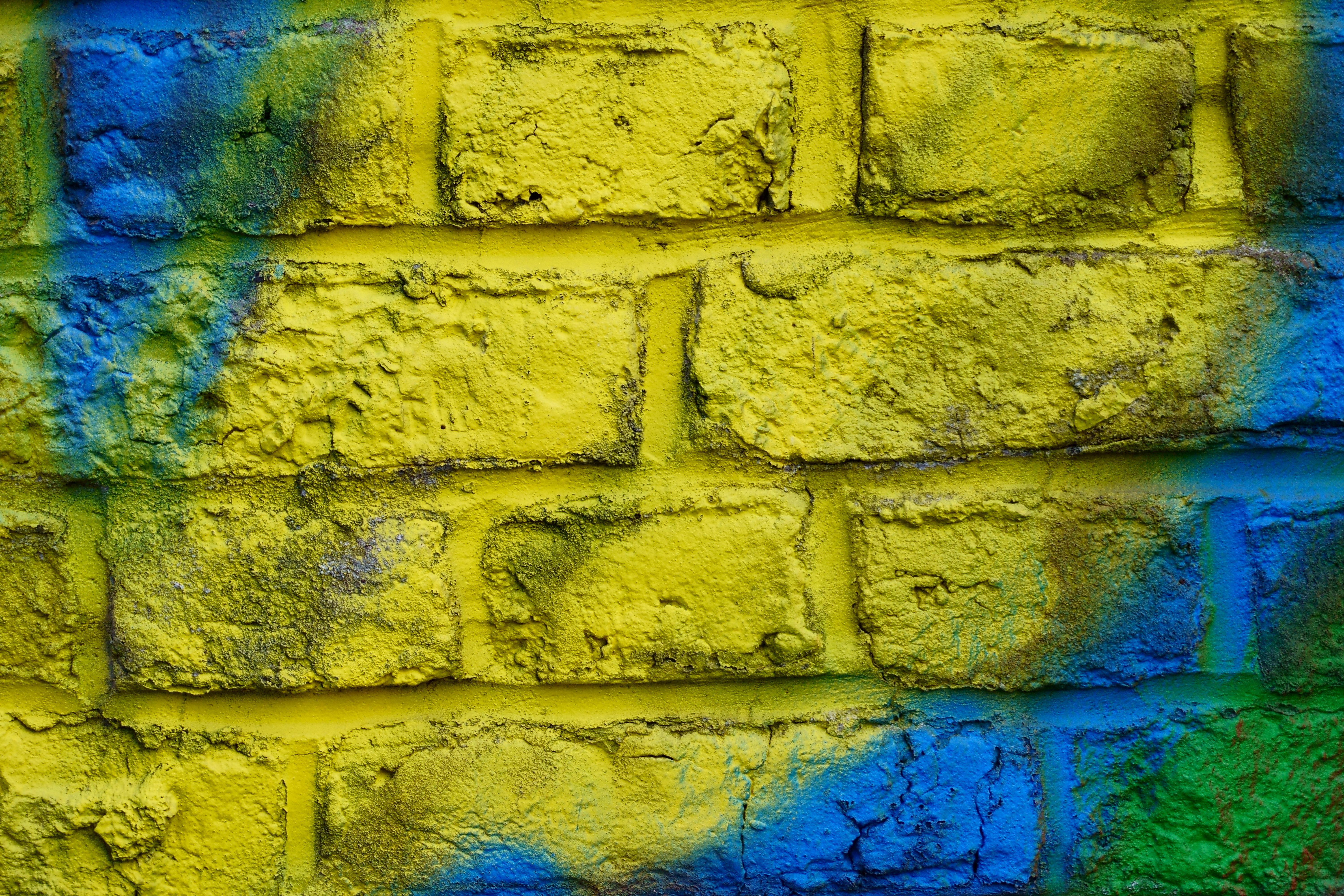 Close-up of a yellow brick wall adorned with blue and green graffiti, showcasing urban street art.