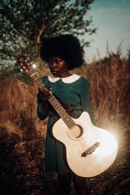 A stylish teenager with a guitar in a sunlit Nigerian meadow, embracing fashion and music.