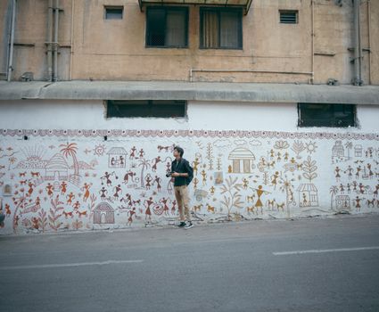 Man stands by vibrant mural on city wall, capturing local street art scene.