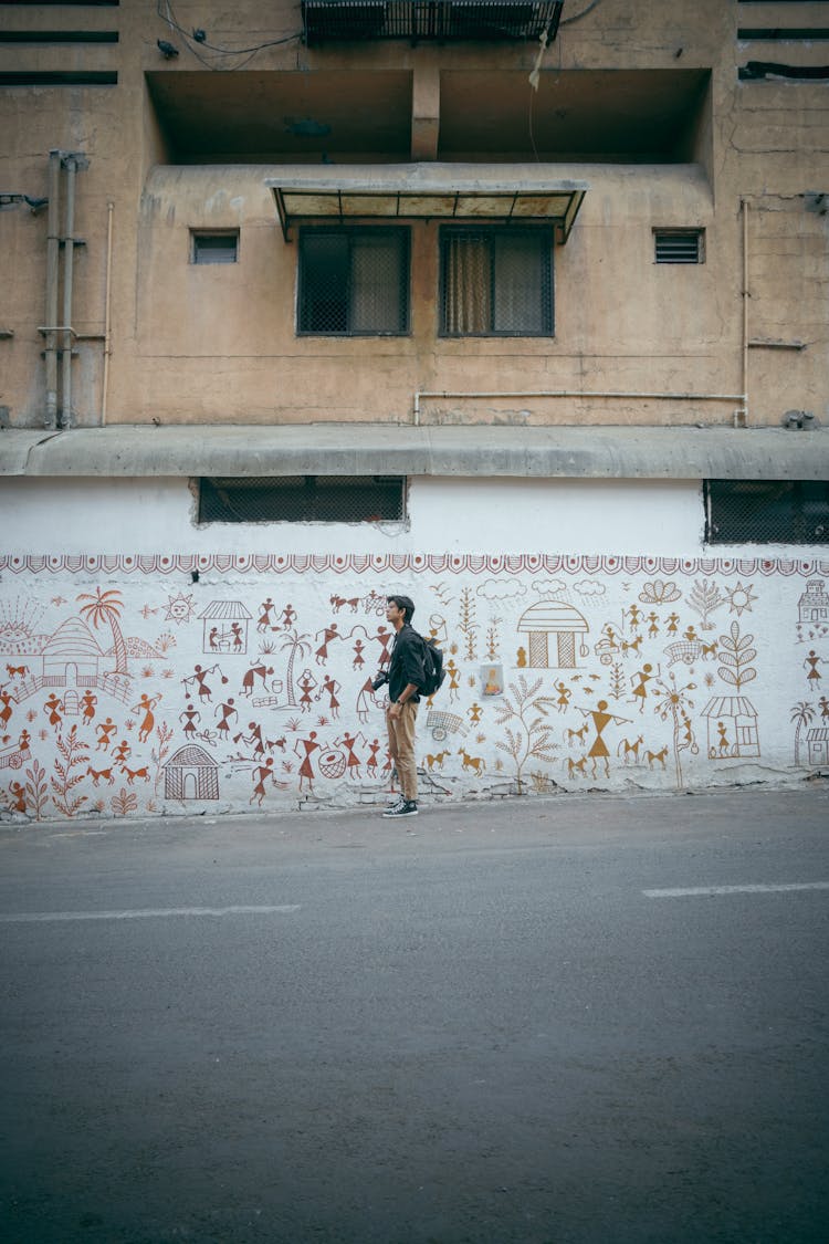 Man Standing In Front Of A Wall And Looking At A Mural Painting 