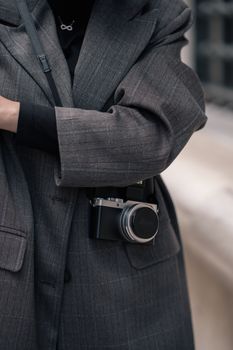 A photographer in a vintage gray overcoat holding a camera on a city street.