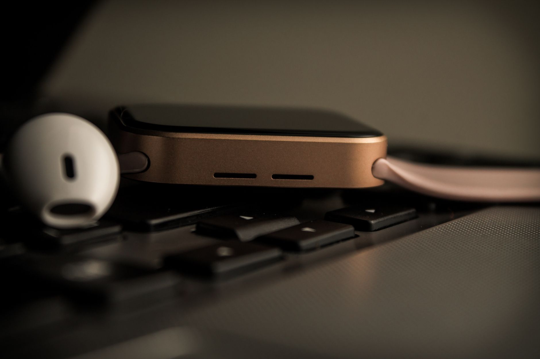 Close-up of a modern smartwatch beside earphones on a laptop keyboard, showcasing contemporary technology.